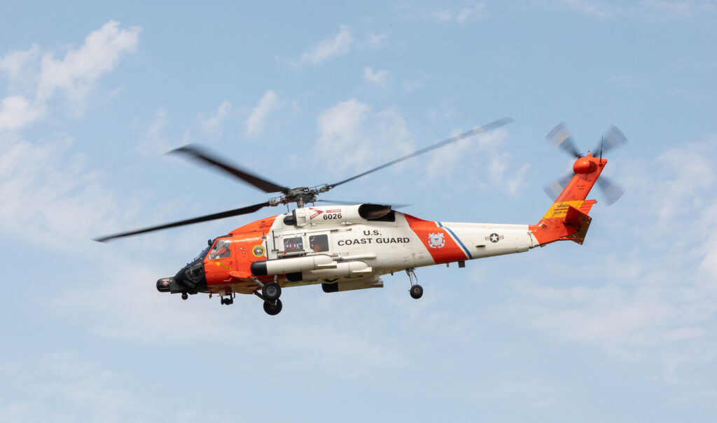 Orange and white U.S. Coast Guard helicopter flying in a blue sky.